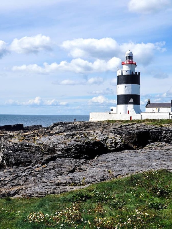 Hook Head Lighthouse on the County Wexford coast, standing above rocky cliffs beside white cottages and the sea.