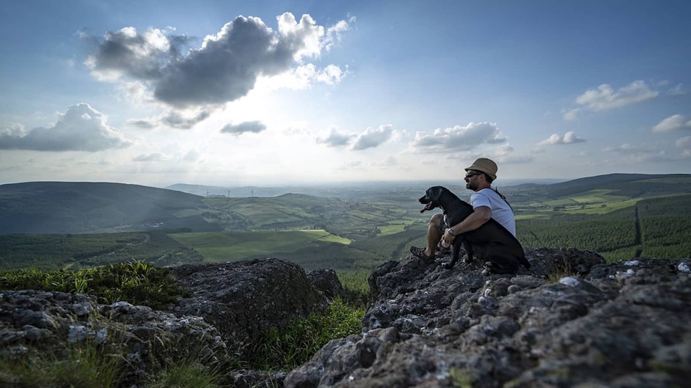 Man sitting with his dog on a rocky viewpoint, overlooking the Devil’s Bit mountains and green countryside in County Tipperary.