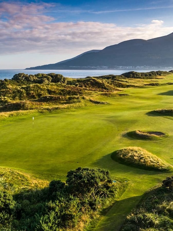 Fairways luxuriants du parcours de golf du Royal County Down avec vue sur la mer et les montagnes Mourne au loin.