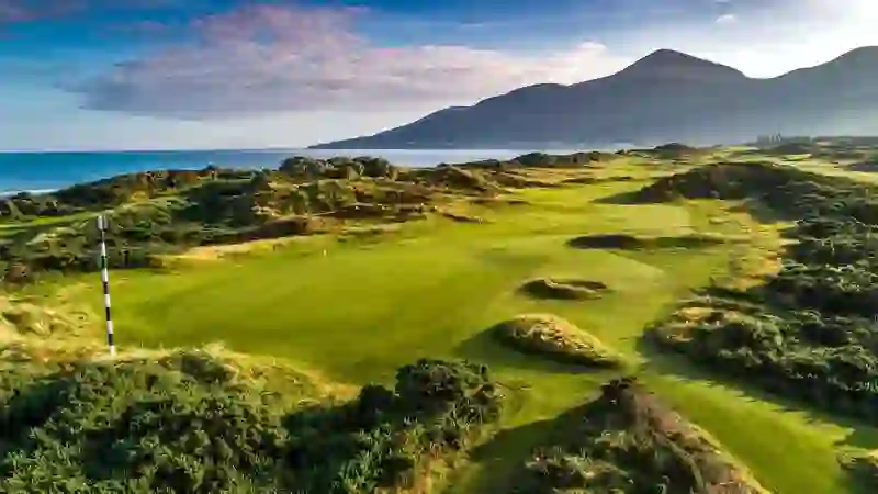 Lush fairways of Royal County Down golf course with sea views and the Mourne Mountains in the distance.