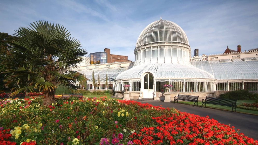 Glass-domed Palm House at Belfast’s Botanic Gardens surrounded by lawns, benches and colourful flowerbeds.