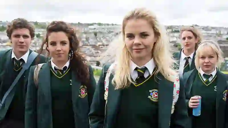 Group of teenagers in green school uniforms standing outdoors with a view of Derry~Londonderry in the background.