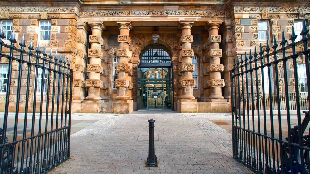 Ornate stone entrance to Crumlin Road Gaol in Belfast, featuring barred gate and dramatic cylindrical columns.