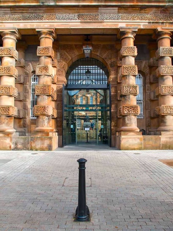 Ornate stone entrance to Crumlin Road Gaol in Belfast, featuring barred gate and dramatic cylindrical columns.