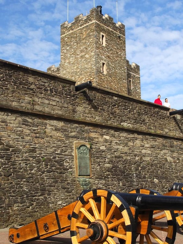 Historic cannons lined along the 17th-century city walls of Derry~Londonderry under a bright blue sky.