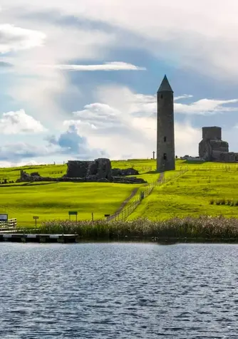 Rundturm und Klosterruinen auf Devenish Island neben einem vor Anker liegenden Boot auf Lough Erne, Grafschaft Fermanagh.