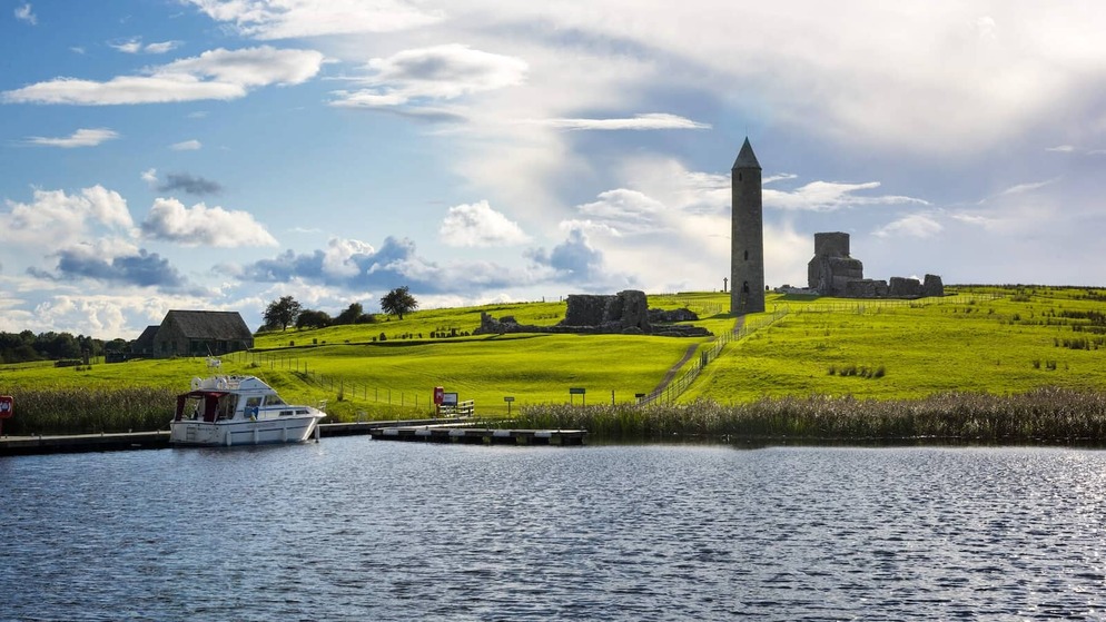 Round tower and monastic ruins on Devenish Island beside moored boat on Lough Erne, County Fermanagh.