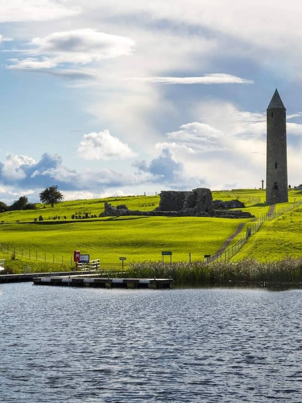 Round tower and monastic ruins on Devenish Island beside moored boat on Lough Erne, County Fermanagh.