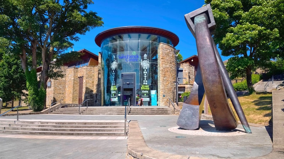 Modern glass and stone entrance of the Saint Patrick Centre with sculpture and summer trees in County Down.