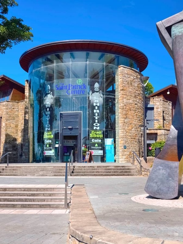 Modern glass and stone entrance of the Saint Patrick Centre with sculpture and summer trees in County Down.