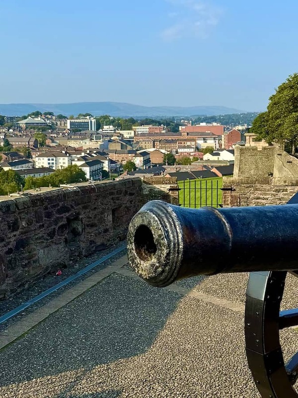 Historic cannon on Derry~Londonderry’s city walls overlooking rooftops and church spires under a blue sky.