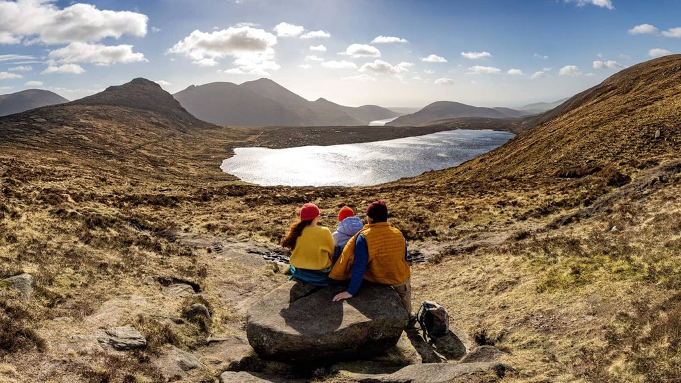 Four hikers looking out over rugged Mourne Mountains in County Down under cloudy skies.