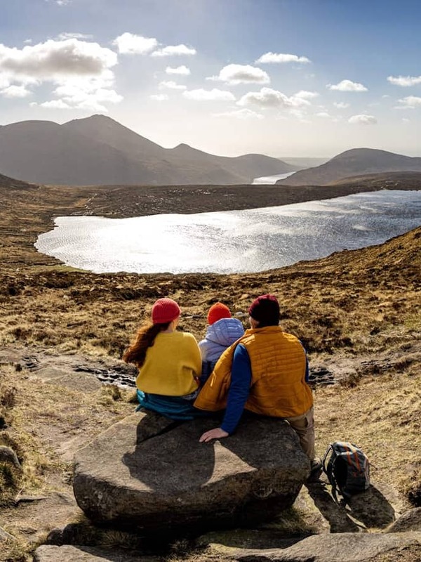 Hikers resting on Mourne Way trail with panoramic view of lakes and Mourne Mountains in County Down, Northern Ireland.