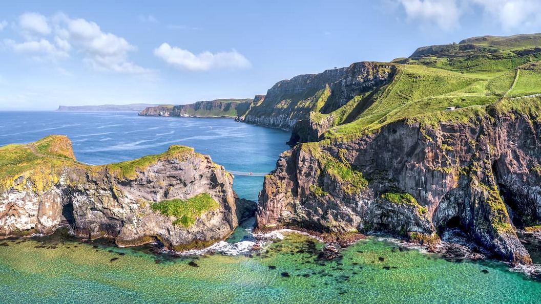 Aerial view of Carrick-a-Rede rope bridge linking rugged cliffs above clear turquoise waters on the County Antrim coast.