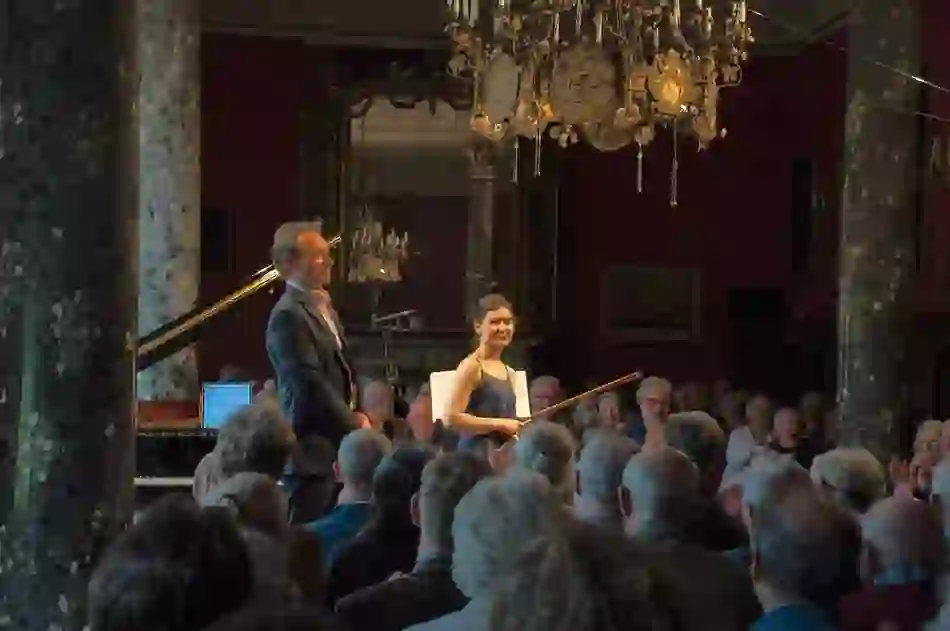 Classical musicians standing before a seated audience in an ornate hall with chandeliers during the West Cork Chamber Music Festival.