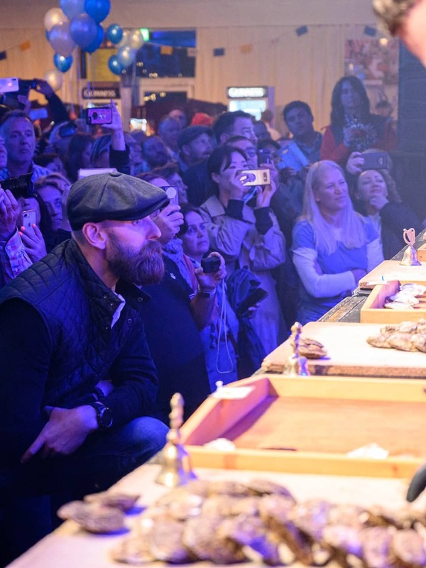 Close-up of oyster shuckers at work while a lively crowd watches at the Galway International Oyster Festival.
