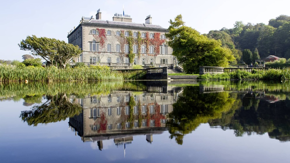 Elegant Westport House in County Mayo reflected in a still lake, surrounded by lush gardens and mature trees.