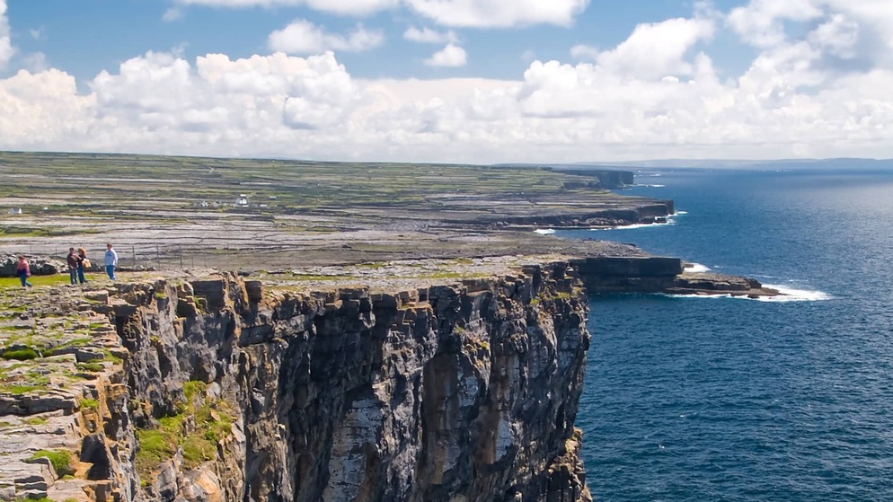 Visitors explore rocky cliffs beside the ancient stone fort of Dún Aonghasa on Galway’s Aran Islands.