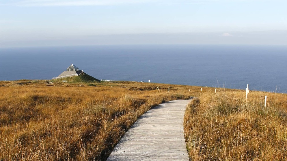 Wooden boardwalk leading through golden moorland to the pyramid-shaped Céide Fields visitor centre overlooking the Atlantic.