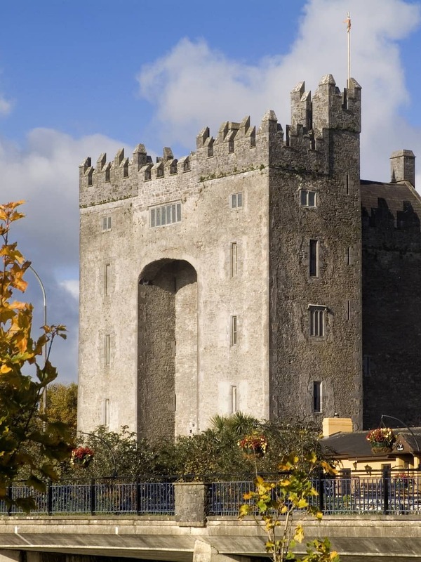 Das mittelalterliche Bunratty-Steinschloss erhebt sich über Herbstbäume, mit seinen befestigten Türmen vor einem strahlend blauen Himmel.