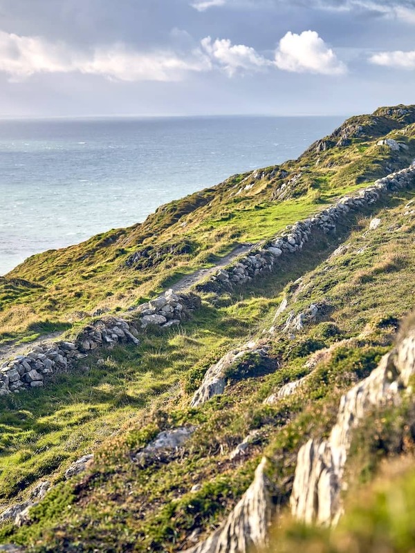 Group of hikers walk a rugged coastal trail on the Sheep’s Head Way in County Cork, overlooking the Atlantic Ocean.
