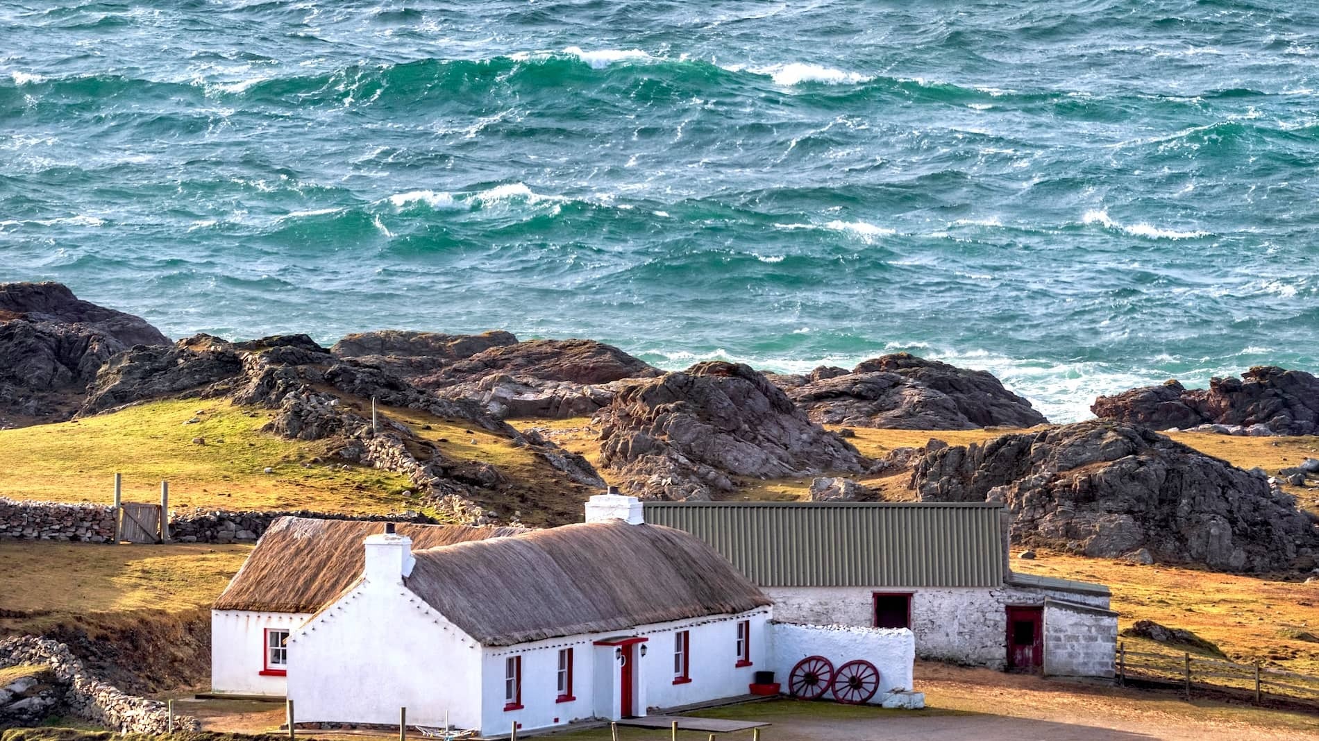 Thatched whitewashed cottage on a rocky headland by the Atlantic Ocean at Malin Head, County Donegal.