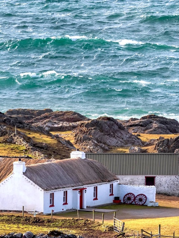 Thatched whitewashed cottage on a rocky headland by the Atlantic Ocean at Malin Head, County Donegal.