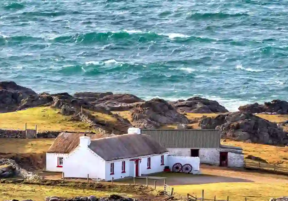 Thatched whitewashed cottage on a rocky headland by the Atlantic Ocean at Malin Head, County Donegal.