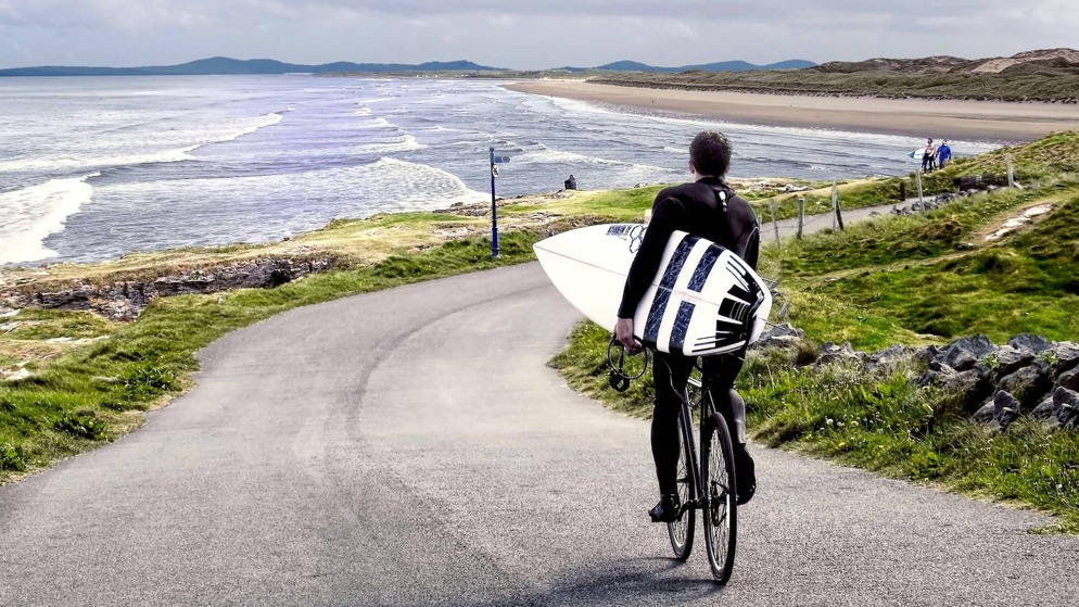 Surfer with board cycling towards the beach at Tullan Strand in Bundoran, County Donegal.