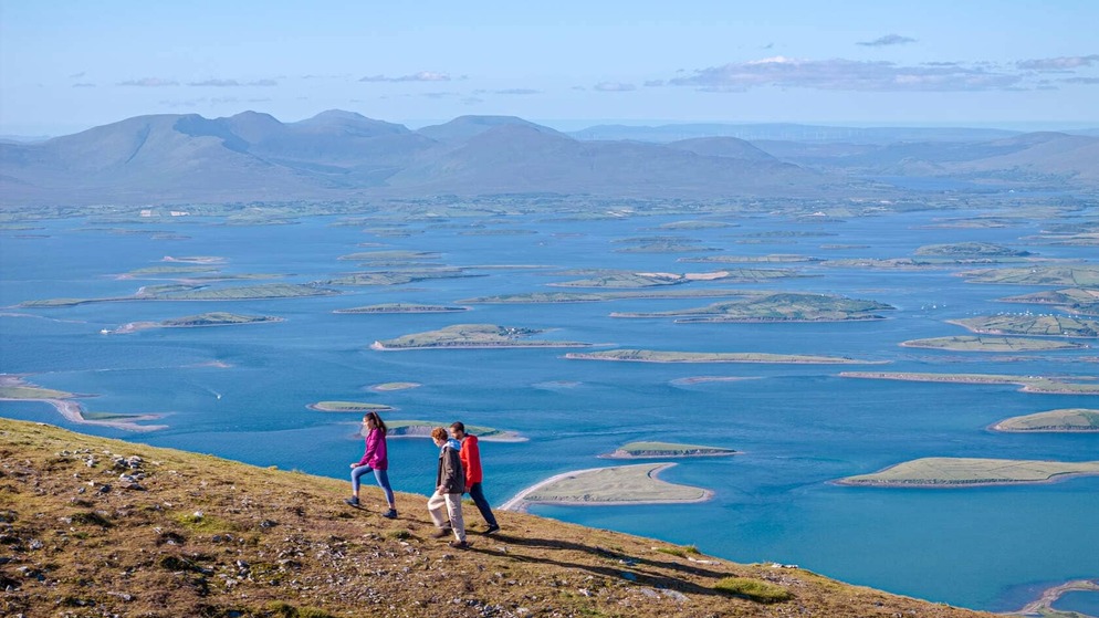 Panoramic view over Clew Bay’s drumlin islands near Westport, with distant mountains rising behind blue Atlantic waters.