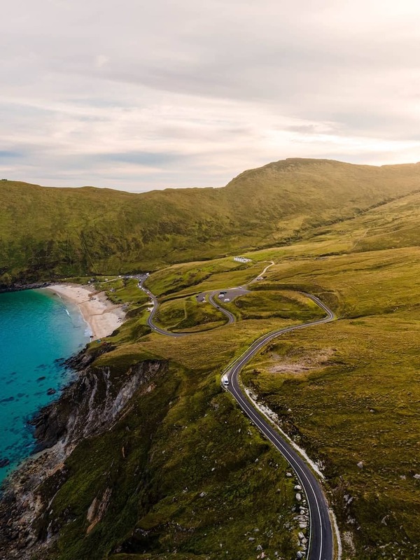 Winding cliff road leading to a golden beach and turquoise sea, backed by grassy hills at Keem Bay, Achill Island, County Mayo.