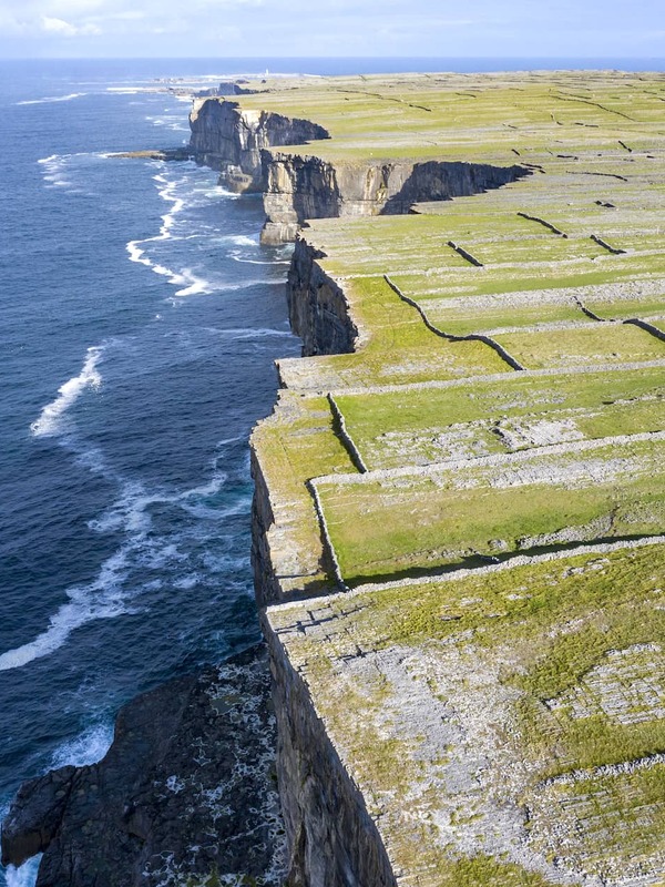 Stone-walled fields stretch to steep sea cliffs on Inis Mór, one of the Aran Islands in County Galway, with deep blue ocean below.