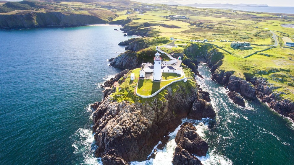 White lighthouse on a rocky Donegal headland, surrounded by dramatic coastline and open Atlantic sea.