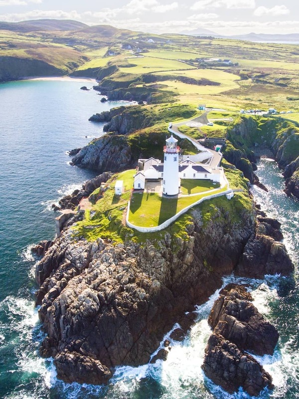 White lighthouse on a rocky Donegal headland, surrounded by dramatic coastline and open Atlantic sea.