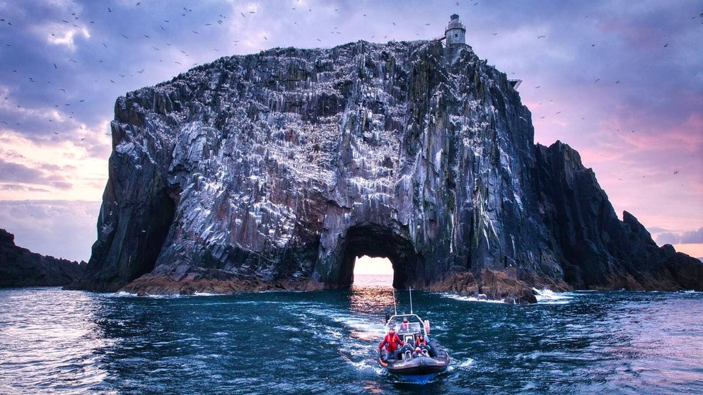 Sunset behind Little Skellig Island off Kerry coast with lighthouse and seabirds circling the rugged sea stack.