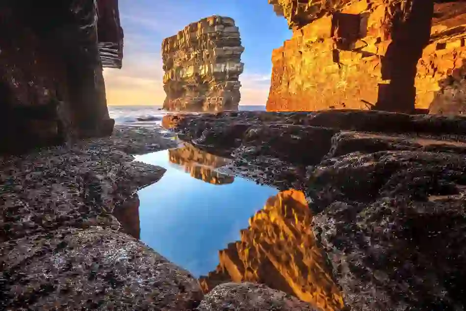 Sea stack at Downpatrick Head reflecting in a tidal pool beneath rugged cliffs on the Mayo coast at sunset.