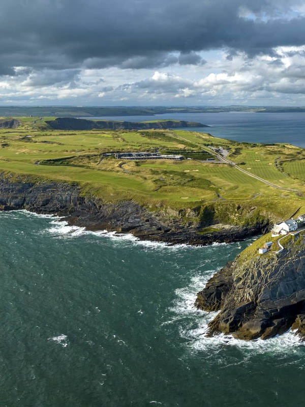 Aerial view of the Old Head of Kinsale lighthouse perched on a dramatic headland jutting into the Atlantic Ocean.