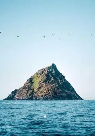 Rocky, grass-covered peak of Skellig Michael rises sharply from the Atlantic, with seabirds soaring overhead.