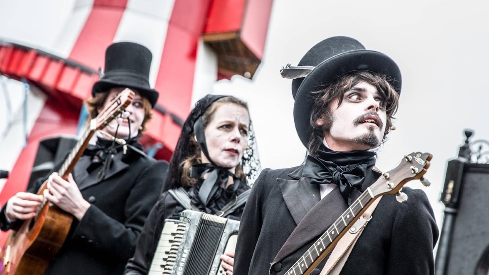 Schauspieler in viktorianischen Gothic-Kostümen treten bei einer Veranstaltung zum Thema Dracula auf und halten Instrumente mit bemalten Gesichtern und Zylindern in den Händen.