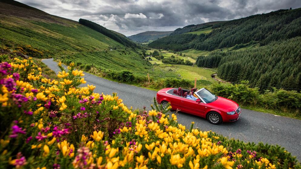 Un descapotable rojo recorre las montañas de Wicklow con flores silvestres y valles ondulantes en la ruta del Ancestral Este de Irlanda.