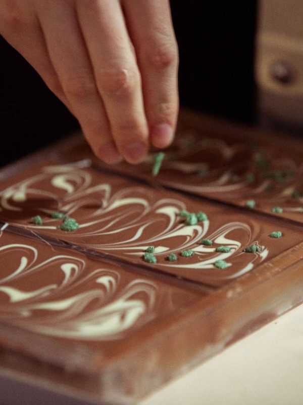 Een hand die toppings strooit op vers gemaakte chocoladerepen met witte krullen.