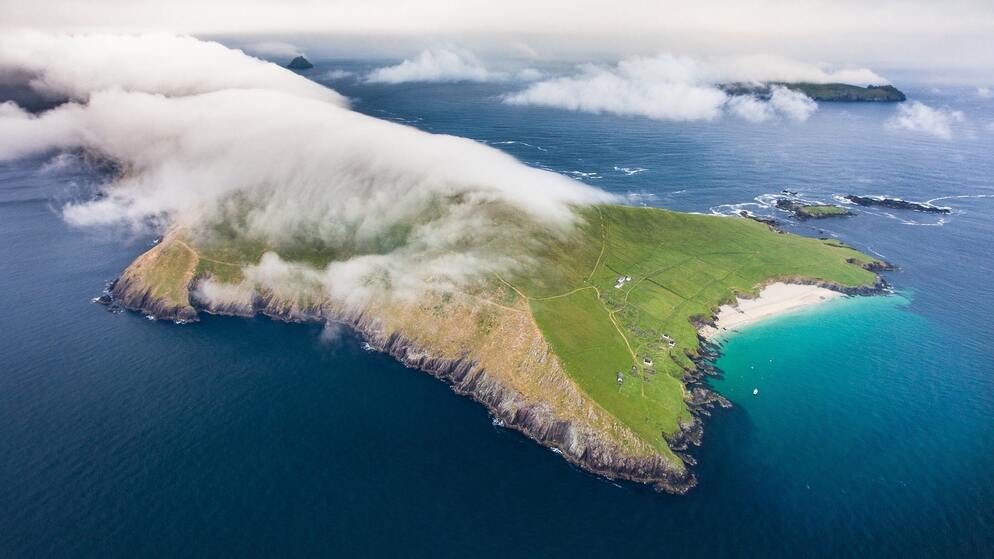 Aerial view of Great Blasket Island off County Kerry, with low-lying cloud, turquoise bay, and rolling green hills meeting the sea.