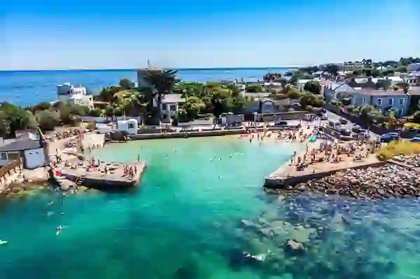Forty Foot bathing area in Sandycove, County Dublin, with swimmers in turquoise sea beside seaside homes.