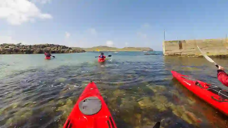 Kayakers paddling through clear turquoise waters near Carrickfinn Beach in County Donegal, Ireland.