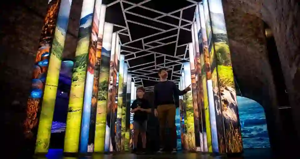 Un homme et un enfant explorent une galerie de panneaux lumineux représentant des paysages irlandais à l'intérieur de l'EPIC, le musée de l'émigration irlandaise.