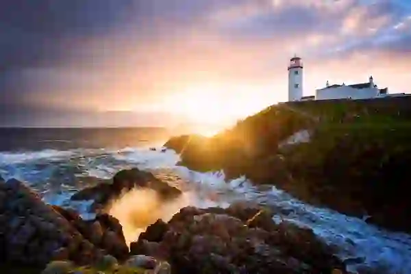 Sunset over Fanad Lighthouse in County Donegal, with waves crashing against the rugged Atlantic coast.