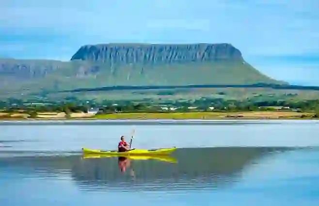 Kayaker paddling on calm water beneath the distinctive flat-topped Ben Bulben mountain in Sligo.
