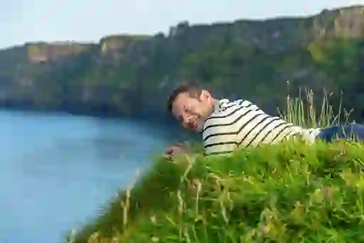 Dermot O'Leary lying on grass near Kinbane Castle cliffs, overlooking the sea and dramatic coastal scenery in Northern Ireland.