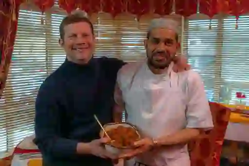 Chef and Dermot O'Leary smiling indoors at Chandpur restaurant in Donegal Town, holding a bowl of freshly prepared curry.