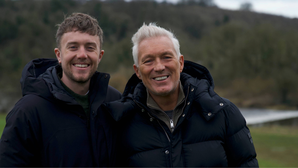 Martin and Roman Kemp smiling beside a forest lake during their Irish road trip.